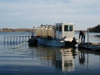 Image slide of HAB’s crew attaches hoses from the large storage tanks at the Public Access to the barge to fill the drums on the barge.
